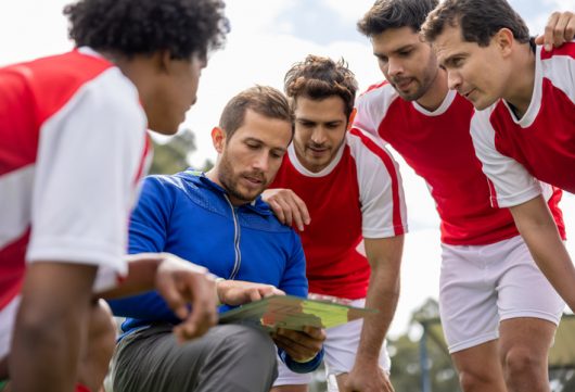 Happy Latin American soccer coach talking to his team about their strategy for the game - sports concepts